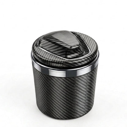 A carbon fiber textured cylindrical container with a matching lid, featuring a polished metallic silver band near the top, set against a plain white background.