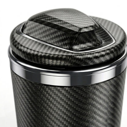 A close-up of car cigarette ashtray with a carbon fiber pattern wrap, featuring a matching lid with a glossy carbon fiber texture and polished silver metal trim.
