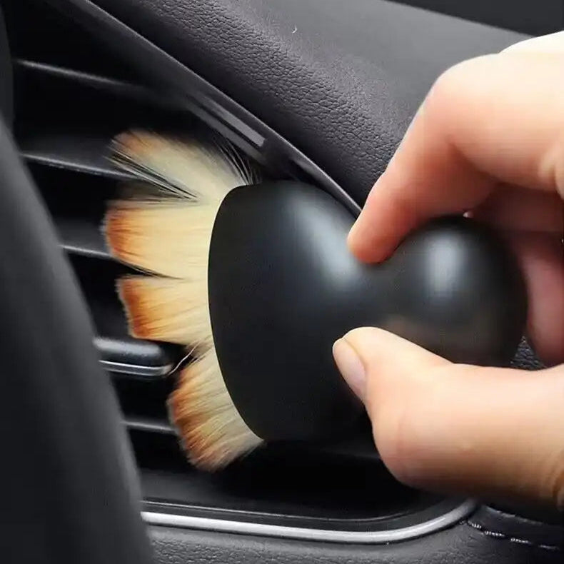 Hand using a car air vent cleaning brush to clean a car's air vent.