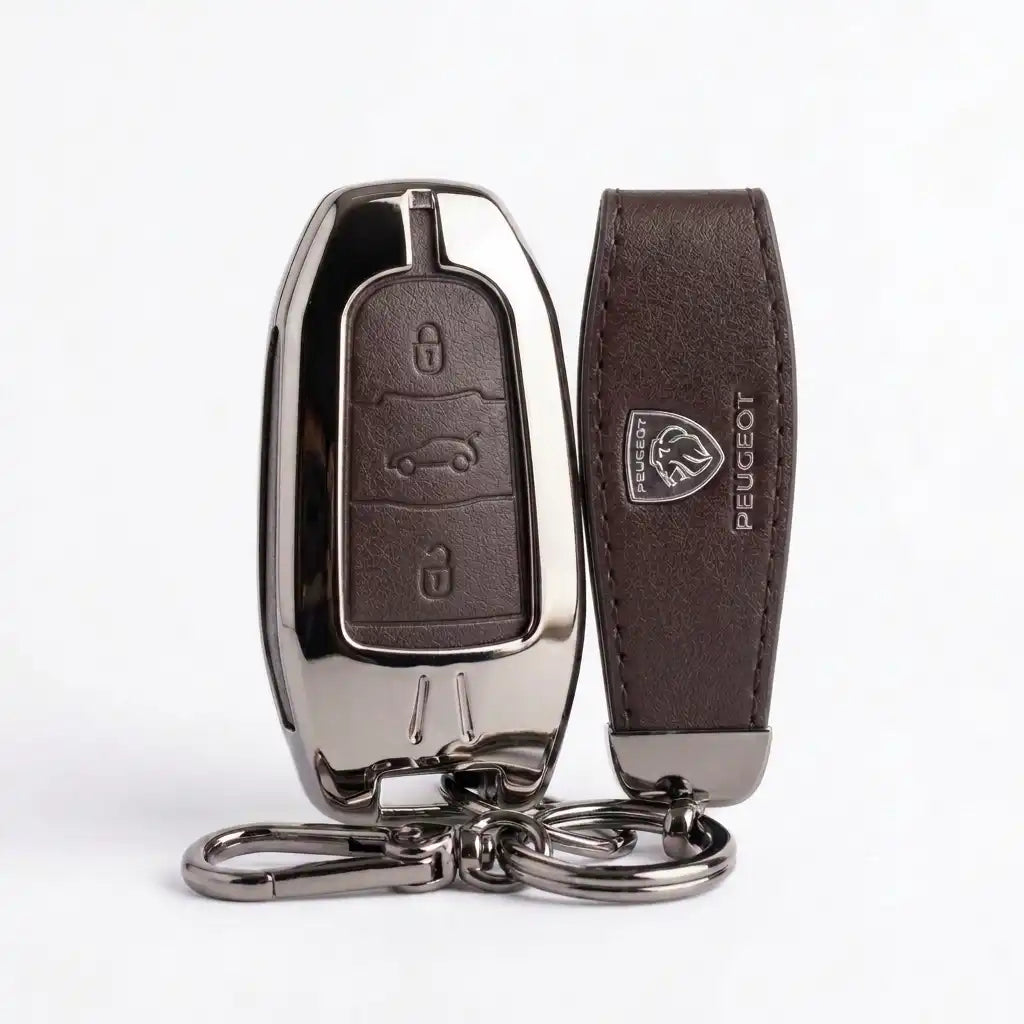 A dark brown leather car key fob cover with a polished chrome metal shell and a matching leather key strap featuring an embossed Peugeot logo, shown on a white background.
