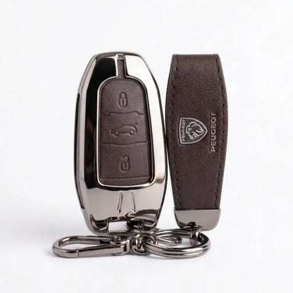 A dark brown leather car key fob cover with a polished chrome metal shell and a matching leather key strap featuring an embossed Peugeot logo, shown on a white background.