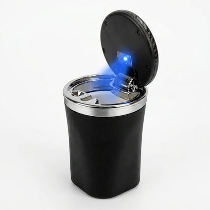 A black cylindrical car ashtray with a hinged lid shown open, featuring a silver metal rim and a glowing blue light on the underside of the lid, set against a plain white background.
